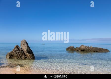 Grande affioramento roccioso su una spiaggia tranquilla, cielo blu calmo e scena oceanica Foto Stock