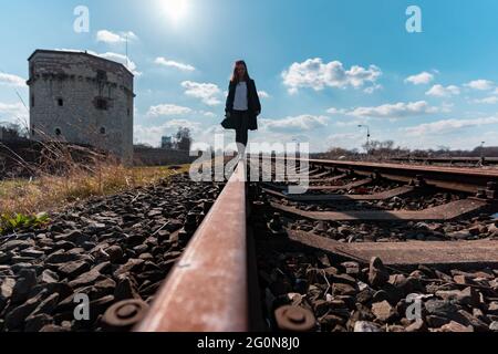 Giovane donna che cammina sulle piste ferroviarie con la torre Kula Nebojsa sullo sfondo Foto Stock