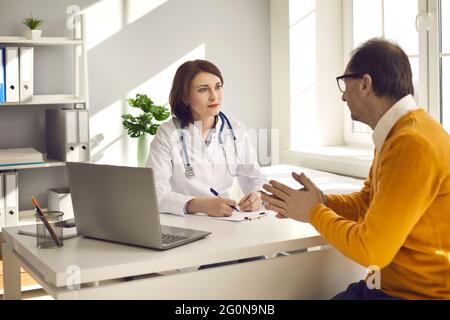 Paziente maschile di mezza età in un reparto ospedaliero consulta una dottoressa sulla sua salute. Foto Stock