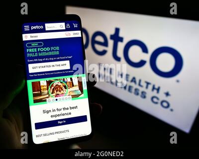 Persona che detiene il telefono cellulare con il sito web del rivenditore statunitense Petco Health and Wellness Company Inc. Su schermo con il logo. Mettere a fuoco il centro del display del telefono. Foto Stock