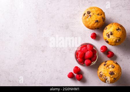 Cupcake dorati appena sfornati e lamponi rossi freschi in vaso su un piano di colore grigio chiaro Foto Stock