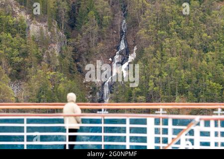 Un passeggero su una nave da crociera che guarda una cascata che scorre lungo una montagna verso l'oceano lungo il passaggio interno, Alaska Foto Stock