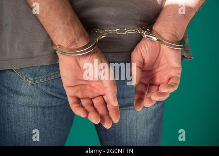 L'uomo arrestato ha manettato le mani sulla schiena. Vista tagliata di un uomo ammanettato in jeans denim isolati sul concetto verde dei diritti umani Foto Stock