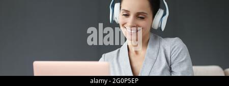 La donna sorridente in cuffia funziona dietro il computer portatile Foto Stock