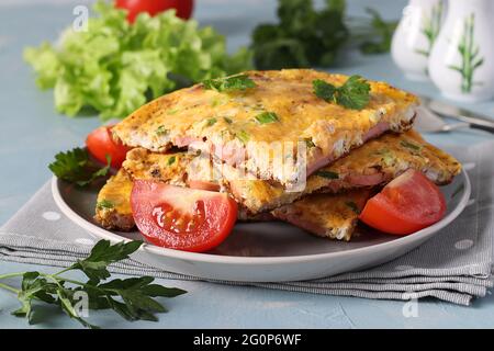 Omelette con salsicce, formaggio e prezzemolo servite con pomodori su un piatto grigio su fondo azzurro. Primo piano. Foto Stock