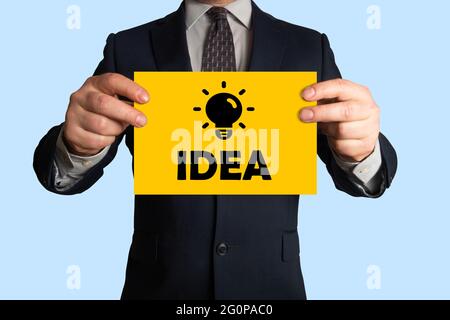 Uomo d'affari che tiene un foglio di carta con l'immagine della lampadina e dell'idea di parola, tutto che simbolizza l'idea, l'innovazione, la creatività, l'ispirazione, innovazione Foto Stock