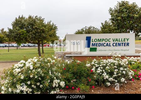 Lompoc, CA, USA - 26 maggio 2021: Emblema bianco su blu sul cartello del numero di strada all'ingresso del Lompoc Valley Medical Center. Auto in parcheggio e piante aggiungere Foto Stock