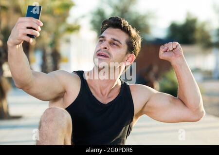 Uomo allegro mostrando bicipiti prendendo selfie Foto Stock