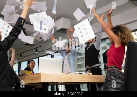 Gruppo di team aziendali che lancia documenti e trionfa con le armi mentre festeggia il successo nell'ufficio di co-working startup Foto Stock