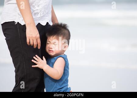 Il bambino asiatico sta in piedi, temendo e abbracciando le gambe della madre mentre si visita il mare per la prima volta Foto Stock