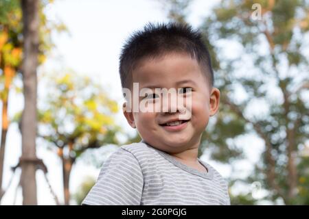 Piccolo ragazzo asiatico in piedi e sorridente felice su sfondo pubblico giardino verde. Un anno, cinque mesi Foto Stock