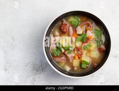 Zuppa di piselli con carni affumicate in un recipiente su sfondo grigio chiaro. Vista dall'alto, disposizione piatta Foto Stock