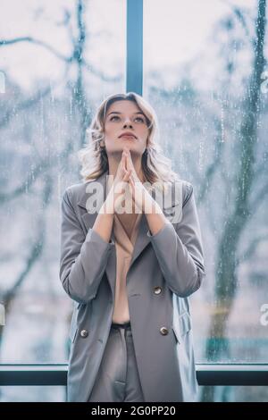 Donna penosa che tiene le palme chiuse vicino al mento Foto Stock