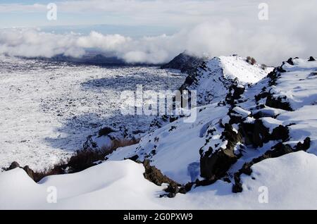 Neve bianca e basse nuvole sul paesaggio della cresta rocciosa 'Salifizio' e della Valle 'Bove' in Sicilia un punto di riferimento del turismo all'aperto nel Parco dell'Etna Foto Stock