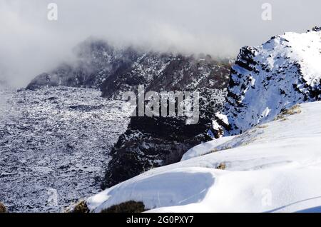 Neve bianca e basse nuvole sul paesaggio della cresta rocciosa 'Salifizio' e della Valle 'Bove' in Sicilia un punto di riferimento del turismo all'aperto nel Parco dell'Etna Foto Stock