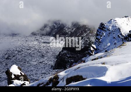 Neve bianca e basse nuvole sul paesaggio della cresta rocciosa 'Salifizio' e della Valle 'Bove' in Sicilia un punto di riferimento del turismo all'aperto nel Parco dell'Etna Foto Stock