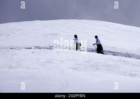 Due escursionisti che camminano attraverso il campo di neve in Sicilia un sentiero di alta montagna per avvicinare la cima dell'Etna punto di riferimento della natura e del turismo all'aperto Foto Stock