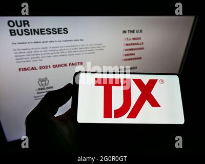 Persona che tiene il cellulare con il logo della società americana di grandi magazzini TJX Companies Inc. Sullo schermo davanti alla pagina web. Mettere a fuoco il display del telefono. Foto Stock