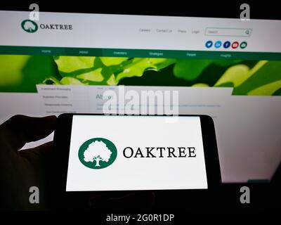 Persona che tiene il cellulare con il logo della ditta americana di investimento Oaktree Capital Management Inc sullo schermo davanti alla pagina web. Mettere a fuoco il display del telefono. Foto Stock