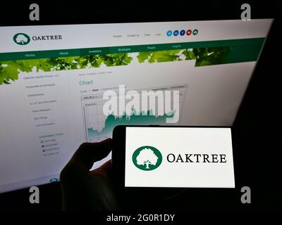 Persona che detiene smartphone con il logo della società di investimento statunitense Oaktree Capital Management Inc. Sullo schermo davanti alla pagina Web. Mettere a fuoco il display del telefono. Foto Stock