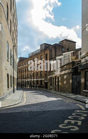 Una strada stretta nel quartiere di Kings Cross di Londra con edifici vittoriani corruti su entrambi i lati della strada acciottolata. Foto Stock