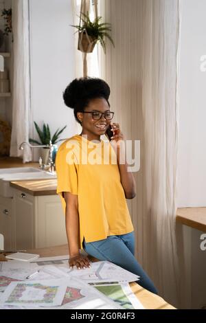 Donna d'affari nera parlare su smartphone, architetto discutere di progetto sul lavoro mobile in remoto a casa Foto Stock