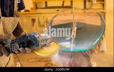 Primo piano di un artigiano africano tavola da surf Shaper lavorare in un'officina di riparazione Foto Stock