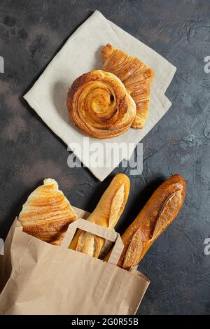 Brioche alla francese, croissant e baguette in un sacchetto di carta eco-compatibile su sfondo scuro, concetto zero sprechi, vista dall'alto Foto Stock