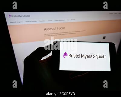 Persona che tiene il cellulare con il logo della società farmaceutica statunitense Bristol Myers Squibb (BMS) sullo schermo davanti alla pagina web. Mettere a fuoco il display del telefono. Foto Stock