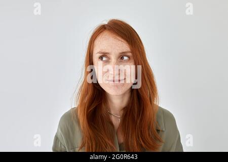 Ritratto di donna felice con capelli zenzero e fracche in piedi su sfondo bianco e guardando via Foto Stock
