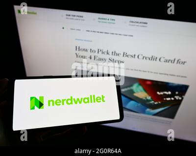 Persona che tiene il cellulare con il logo della società americana di finanza personale NerdWallet Inc. Sullo schermo di fronte al sito web aziendale. Mettere a fuoco il display del telefono. Foto Stock