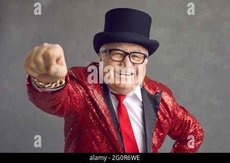 Studio ritratto di divertente ricco vecchio in occhiali, giacca in paillettes e cappello nero Foto Stock