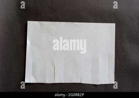 Foglio bianco vuoto con linguette a strappo su sfondo grigio. Foglio di carta sgualcito con strisce irregolari. Tutti i segnalibri a strappo. Nuovo o unint Foto Stock