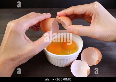 Chiocciolare le mani dell'uomo che spezzano l'uovo in una ciotola Foto Stock