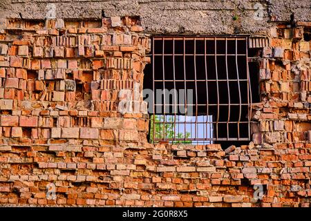 Grata di metallo nel muro di mattoni della casa distrutta; cielo blu attraverso la barriera Foto Stock
