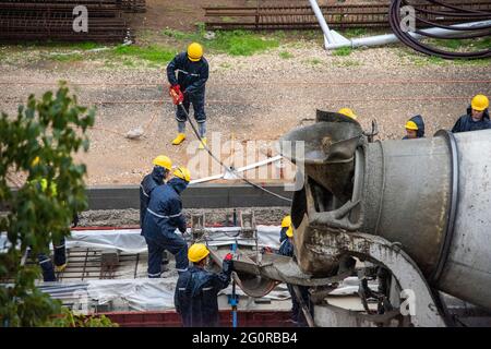 Tel Aviv, Israele - Maggio 20 2021: Lavoratori edili che lavorano sotto la pioggia. Guide leggere. Operaio con collare blu. Collaborazione concettuale. Camion, betoniera, bulldozer. Foto di alta qualità Foto Stock