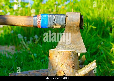 Tritare il legno con una vecchia ascia metallica o con un manico in legno in natura. Grumo di pino su erba verde. In estate giorno. Vita rurale, una casa Foto Stock