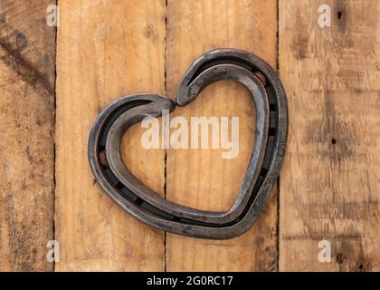 Romantico amore cuore a forma di scarpa da cavallo creato da farrier posato su rustico vintage tavola di legno sfondo. Foto Stock