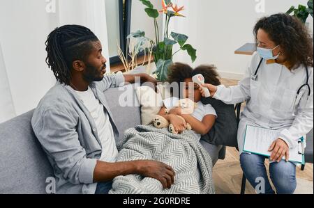 La casa chiama i medici. Pediatra misura la temperatura di una bambina paziente con raffreddore e influenza utilizzando un termometro a infrarossi a casa. assistenza medica a h Foto Stock