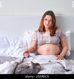 Donna incinta solitaria si trova nel letto accanto al suo animale domestico Foto Stock