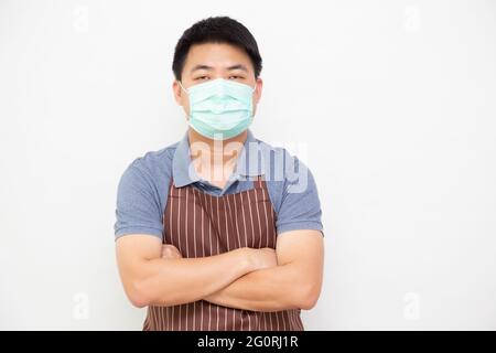 Ritratto dei lavoratori asiatici mercato fresco con grembiule marrone indossare maschera medica di protezione per prevenire il virus e in piedi con le braccia incrociate su w Foto Stock