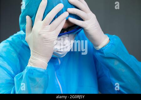 Il medico che indossa l'uniforme PPE è stressato e mal di testa dopo un lungo turno di lotta contro Coronavirus SARS-COV-2 Foto Stock