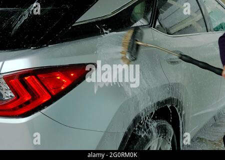 Uomo che lava un'auto con una spazzola che sparge lo shampoo sopra di essa. Una scena da autolavaggio self service. Foto Stock