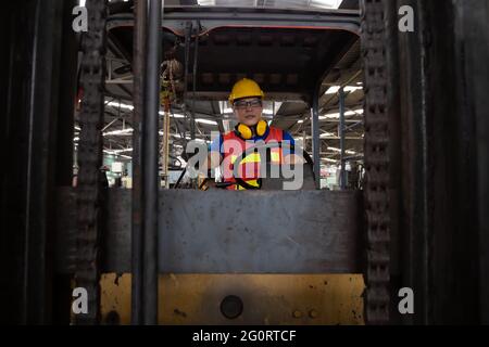 Conducente asiatico di carrelli elevatori sul posto di lavoro in fabbrica e guardando la telecamera Foto Stock