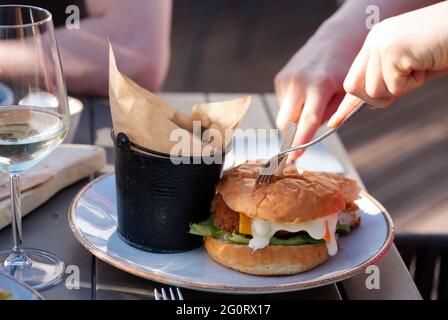 Gruppo di amici che tostano bicchieri di birra e vino e mangiano hamburger in ristorante. adulti in un pub con hamburger e bevande Foto Stock