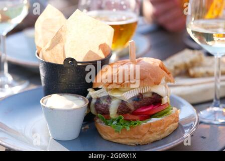 Gruppo di amici che tostano bicchieri di birra e vino e mangiano hamburger in ristorante. adulti in un pub con hamburger e bevande Foto Stock