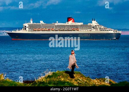 Una donna gode di una vista della magnifica nave da crociera Queen Mary 2 con nave da crociera ancorata al largo di Torbay in Devon, Regno Unito. Foto Stock