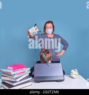 Divertente ragazzo junior in divisa scolastica alla sua scrivania con il computer portatile, problemi di apprendimento a distanza a causa del coronavirus Foto Stock