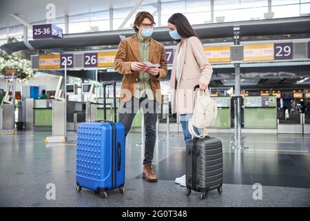 Giovane uomo e donna in maschere mediche per il check-in in aeroporto Foto Stock