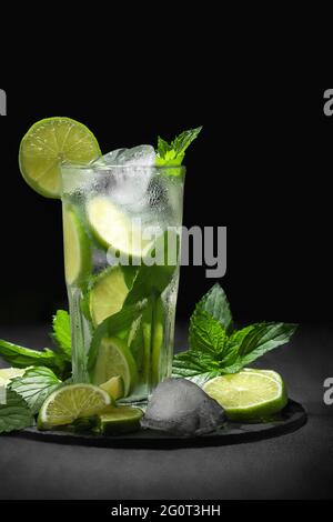 Fresco cocktail mojito fatto in casa in un bicchiere alto con lime, menta e ghiaccio su sfondo nero, spazio copia, immagine verticale. Foto Stock